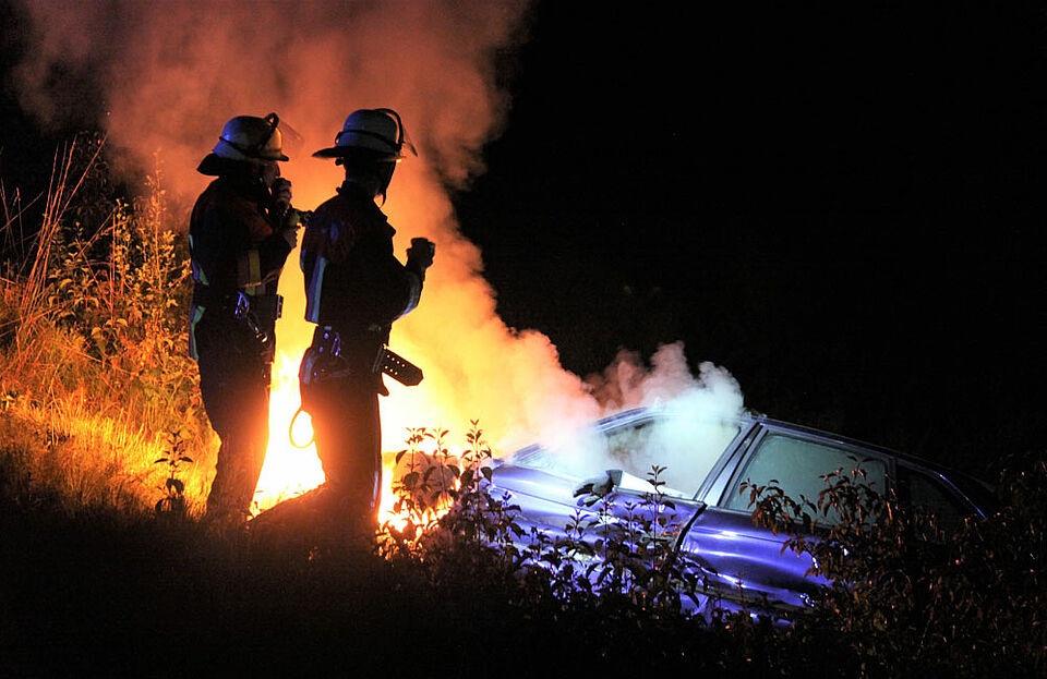 Gespenstische Szenen boten sich bei absoluter Dunkelheit den ersten Einheiten von Feuerwehr und Rettungsdienst am Unglücksort. Ein Pkw wurde neben die Gleise an eine Böschung geschleudert und stand in Flammen. Der eingeklemmte Fahrer (simuliert von einer Puppe), dessen linker Arm aus dem Fahrerfenster hängt, hatte keine Überlebenschance. (Foto: Michael Will / BRK)