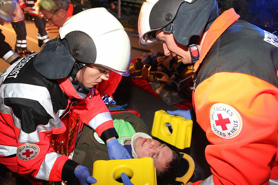 Ein Rettungsteam versorgt einen Patienten und führt eine Ganzkörper-Immobilisation durch. Der Mann war zuvor zusammen mit zwei anderen Insassen in einem Auto eingeklemmt und schwer verletzt. (Foto: Michael Will / BRK)