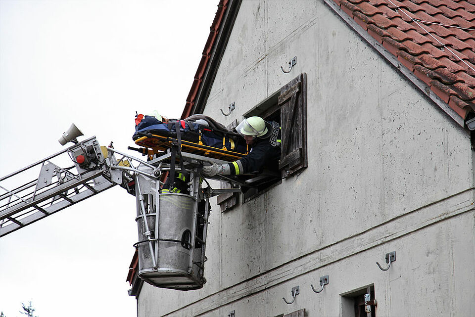 Aus dem Obergeschoss des Übungshauses wird eine Person mithilfe der Drehleiter der Feuerwehr Ebern gerettet und auf sicheren Boden gebracht.